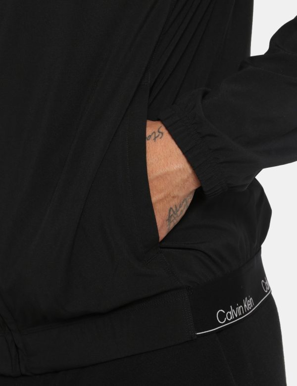 Giacca Calvin Klein Nero - Giacca leggera in total nero con cappuccio. Presenti tasche a taglio trasversale più logo brand b