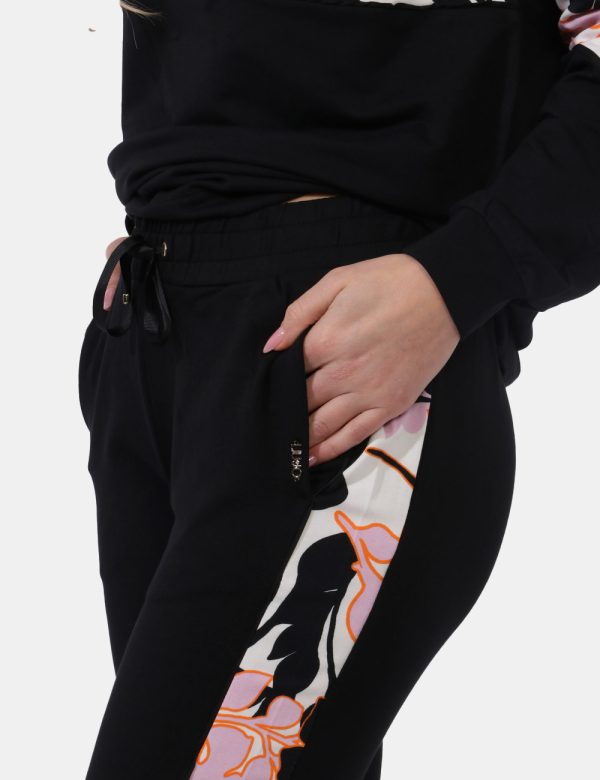 Pantaloni Liu-Jo Nero - Pantaloni tuta in total nero con bande laterali floreali in tinta tendente al rosa. Presenti tasche