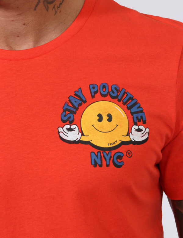 T-shirt Fred Mello Arancione - T-shirt su base arancione con stampa smile in giallo e blu. La vestibilità è morbida e regola