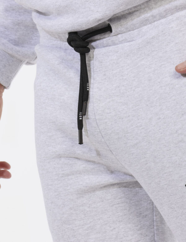 Pantaloni Icon Grigio - Pantaloni simil tuta grigio chiaro con logo brand nero. Presenti tasche a taglio trasversale. La ves