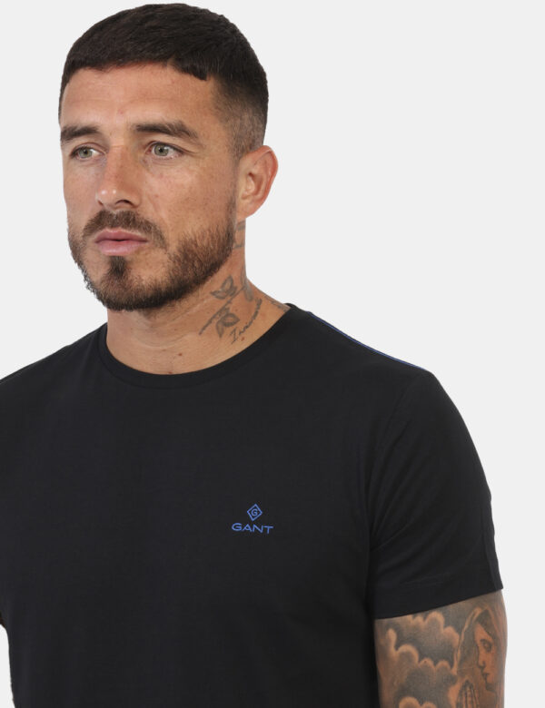 T-Shirt Gant Nero - T-shirt classica in total nero con patch logo brand ad altezza cuore in blu. La vestibilità è morbida e