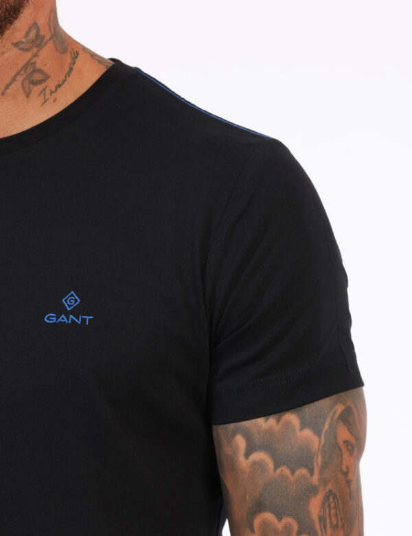 T-Shirt Gant Nero - T-shirt classica in total nero con patch logo brand ad altezza cuore in blu. La vestibilità è morbida e