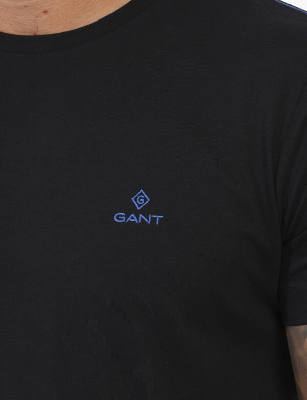 T-Shirt Gant Nero - T-shirt classica in total nero con patch logo brand ad altezza cuore in blu. La vestibilità è morbida e
