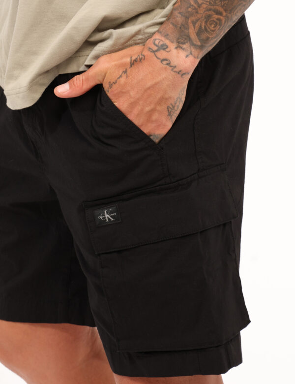 Bermuda Calvin Klein Nero - Bermuda in total nero con tasche a taglio trasversale e tasche cargo laterali. La vestibilità è