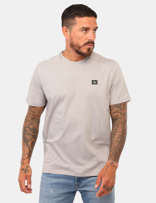 T-shirt Calvin Klein Grigio - T-shirt classica in total grigio chiaro con patch logo brand nero. La vestibilità è morbida e