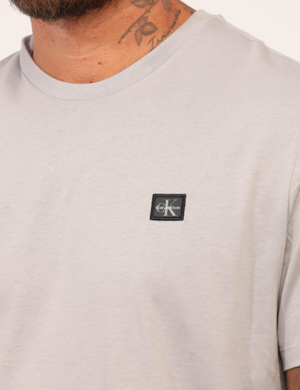 T-shirt Calvin Klein Grigio - T-shirt classica in total grigio chiaro con patch logo brand nero. La vestibilità è morbida e