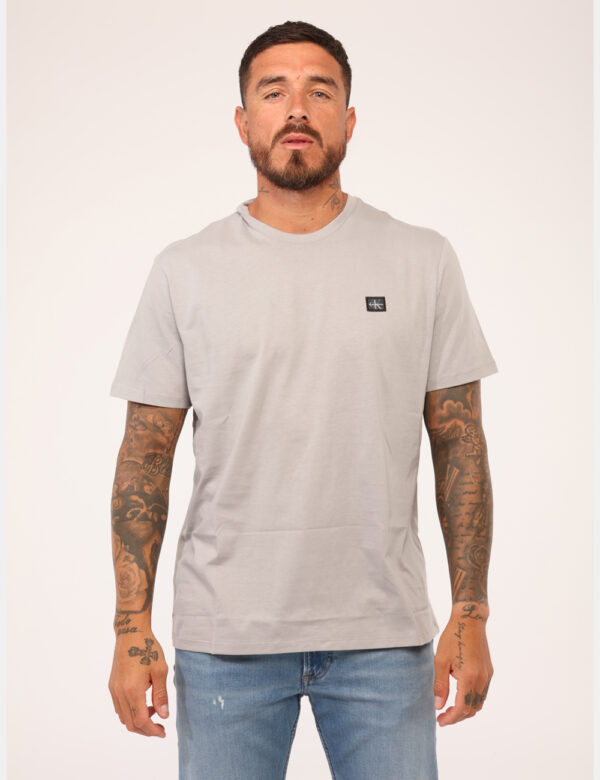 T-shirt Calvin Klein Grigio - T-shirt classica in total grigio chiaro con patch logo brand nero. La vestibilità è morbida e